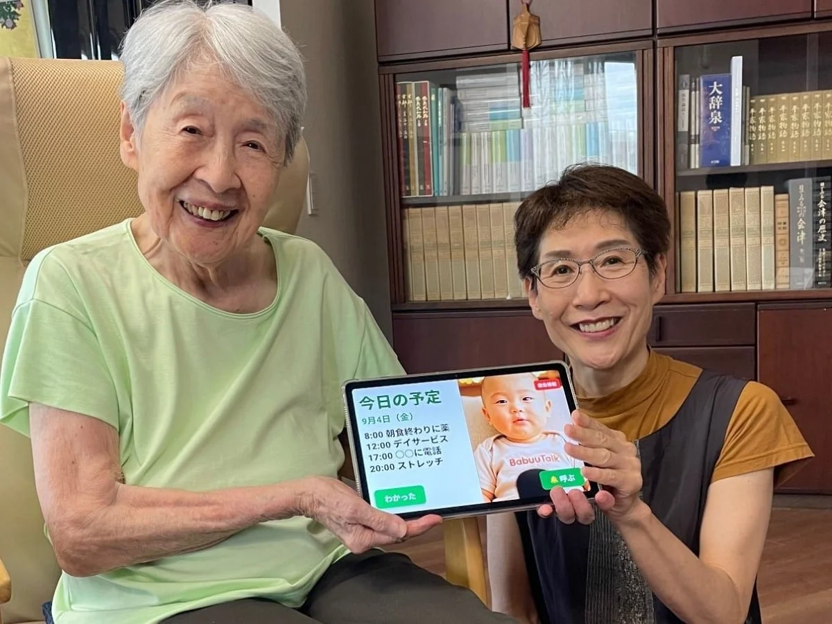 高齢女性と中年の女性が笑顔でタブレットを掲げている画像